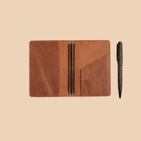 Brown leather notebook with pen on a beige background