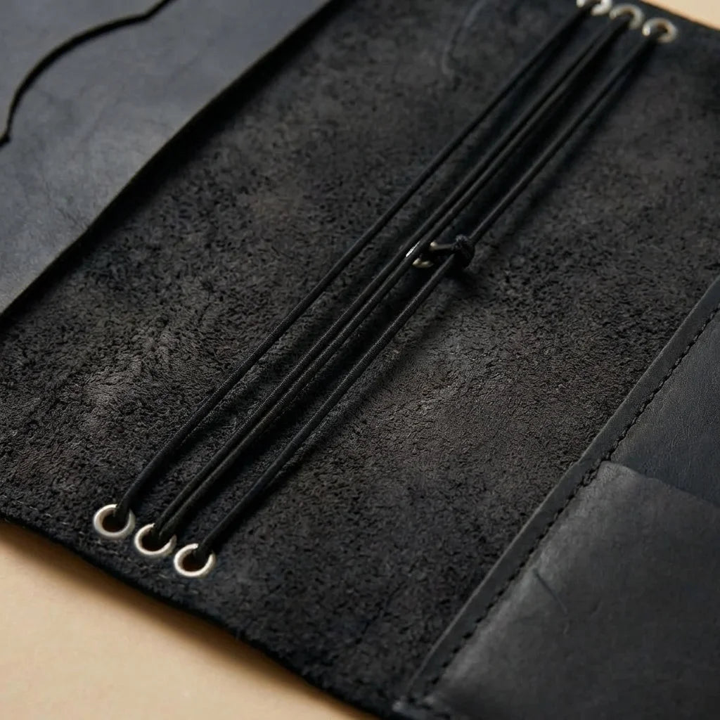 Close-up of a black leather journal with metal loops on a beige surface