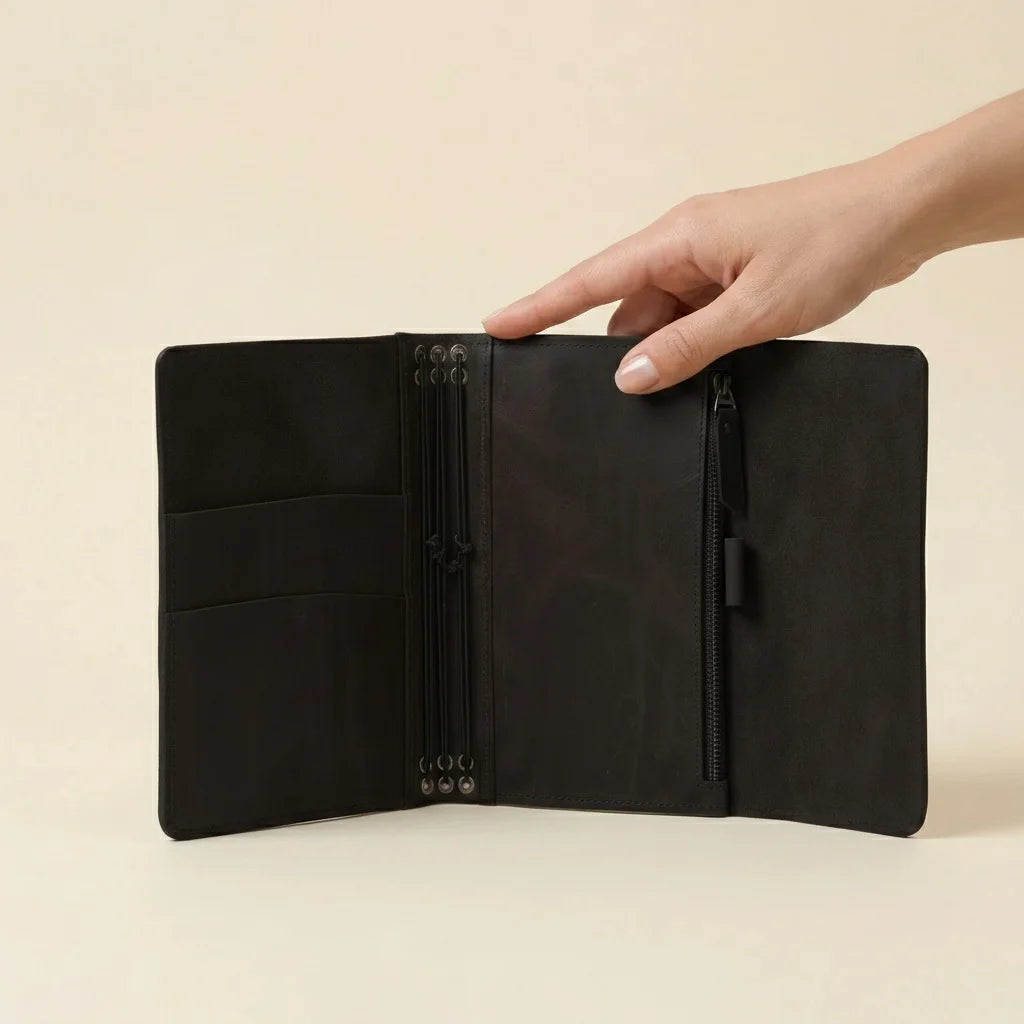 Black leather journal held open by a hand on a beige background
