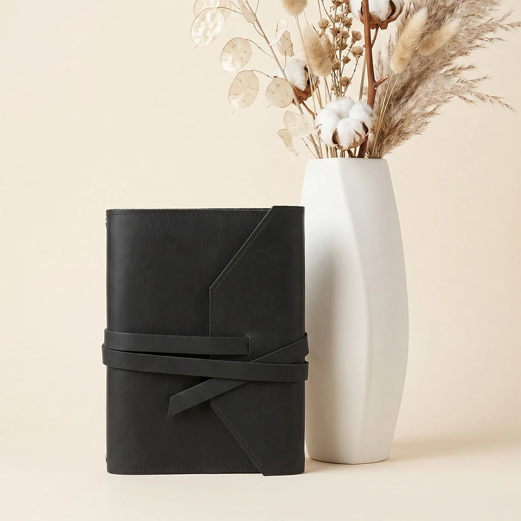 Refillable notebook cover in leather with secure straps and pen loop attachment.