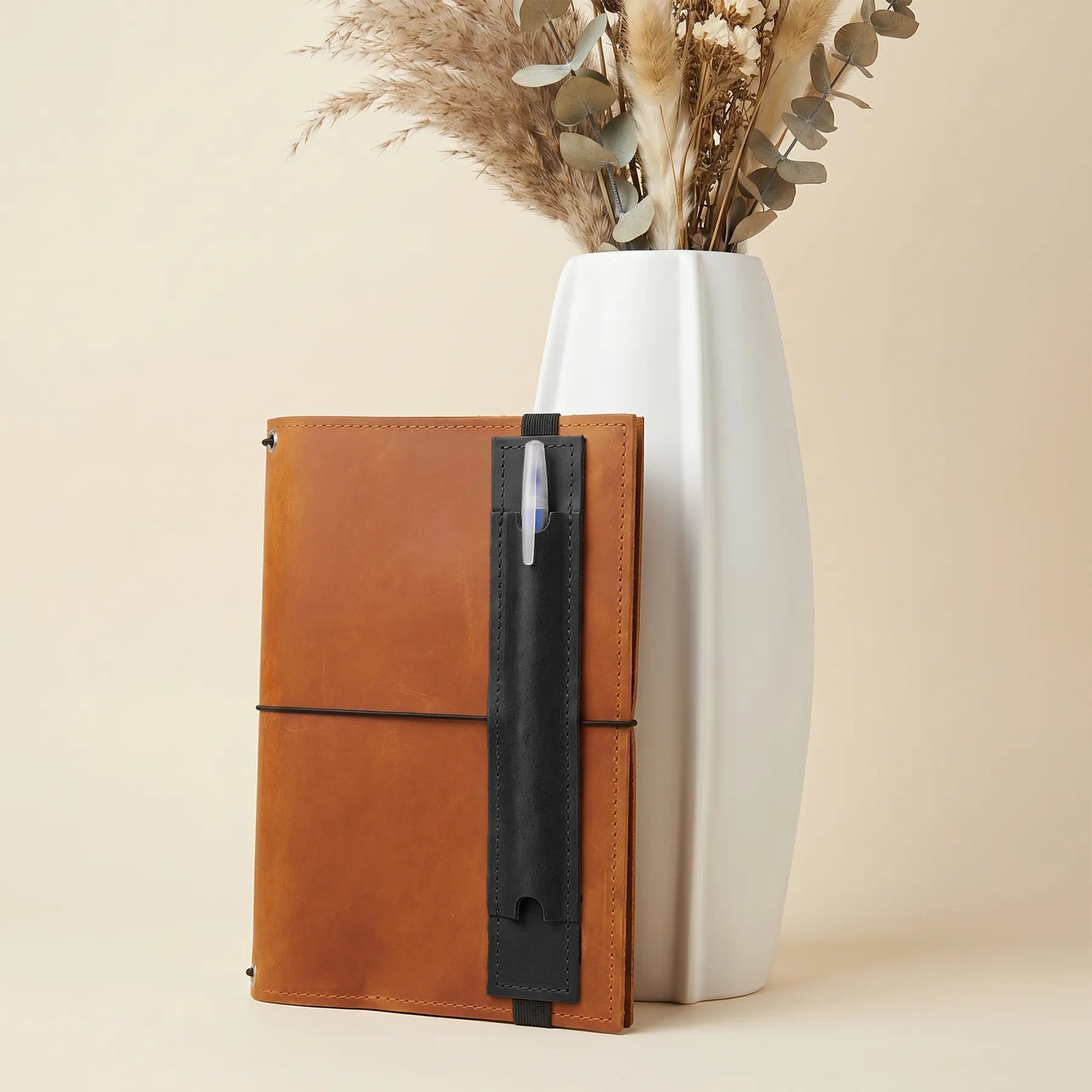 Genuine leather notebook pen holder combining minimalist design with practical elastic band attachment.
