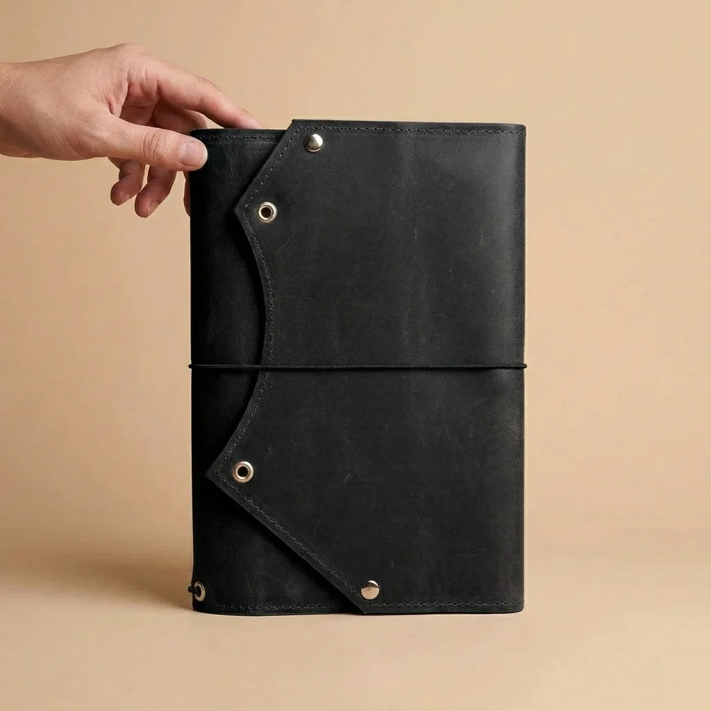 Black leather notebook held by a hand on a beige background