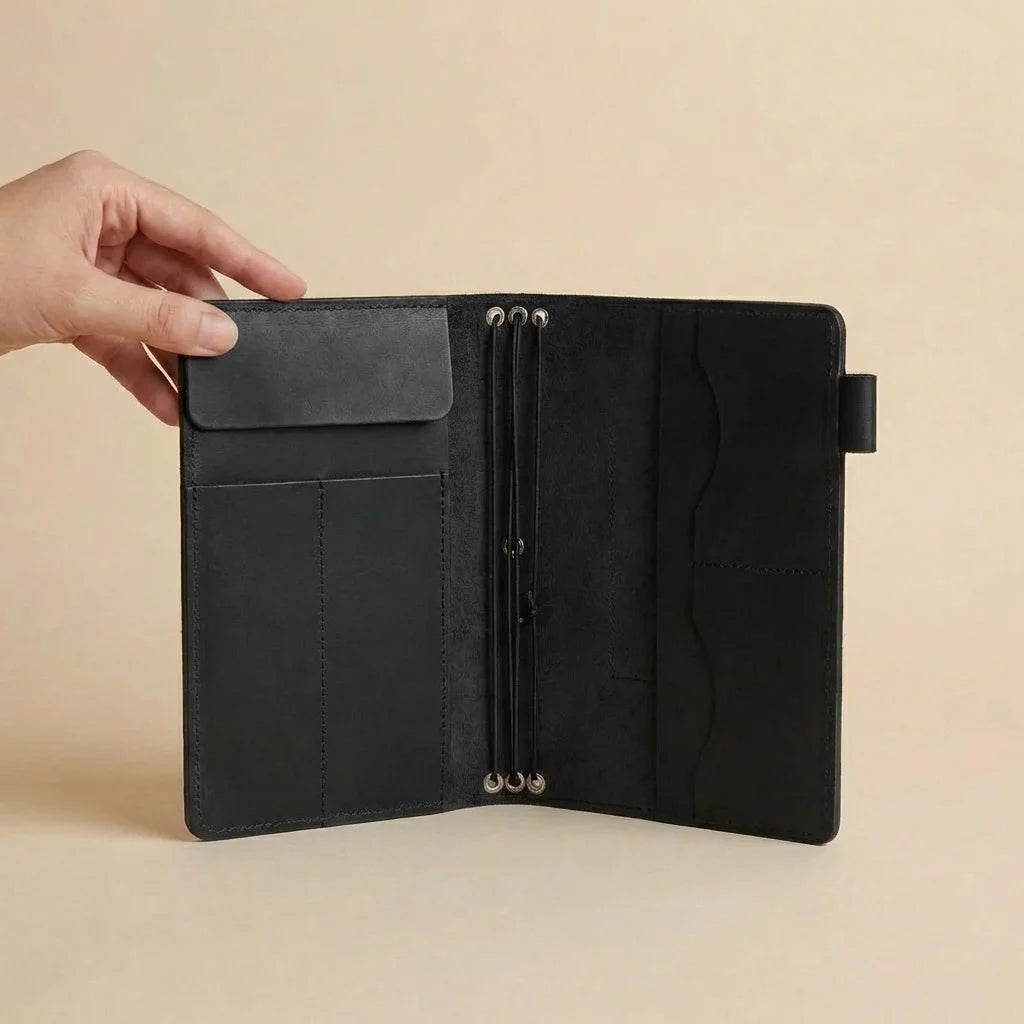 Black leather journal held open by a hand on a beige background