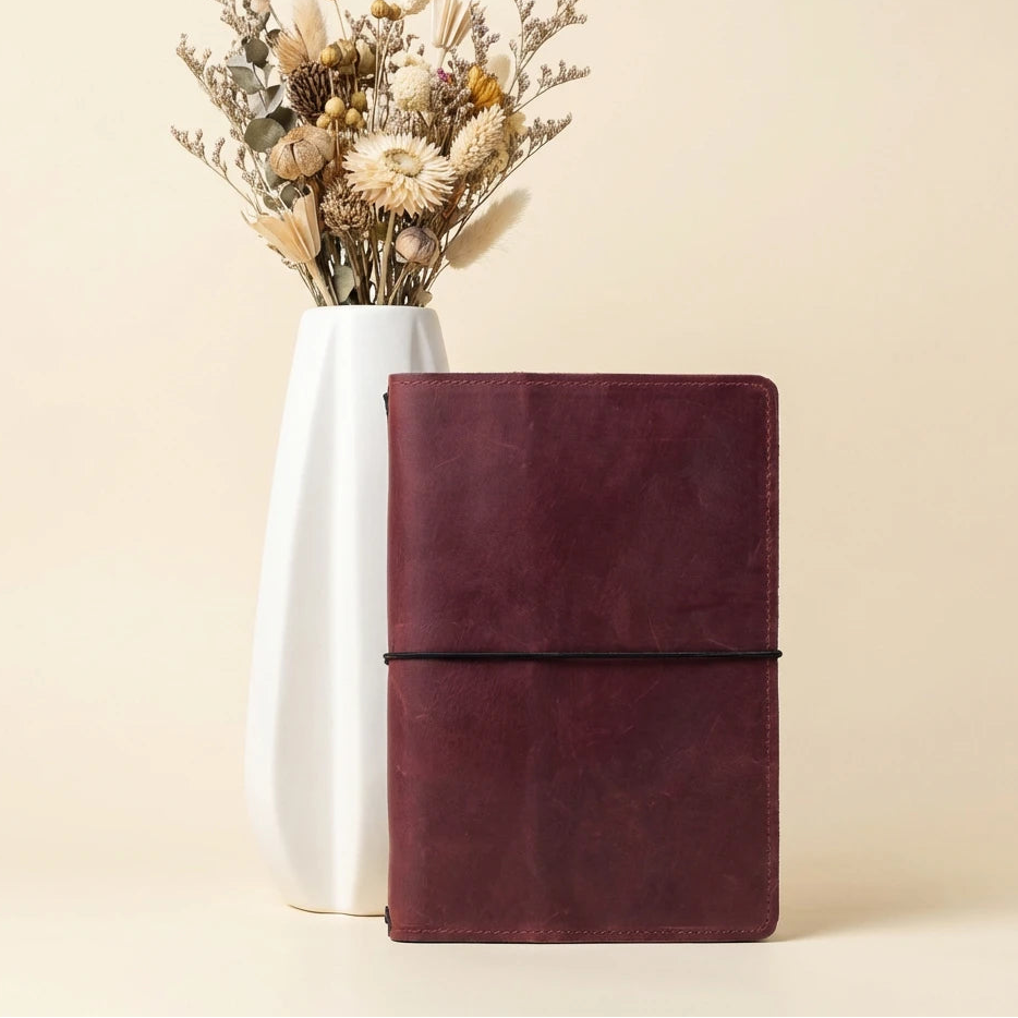 Brown leather notebook next to a white vase with dried flowers on a beige background