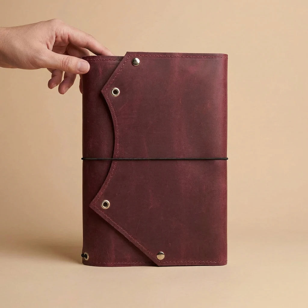 Hand holding a maroon leather-bound notebook against a beige background