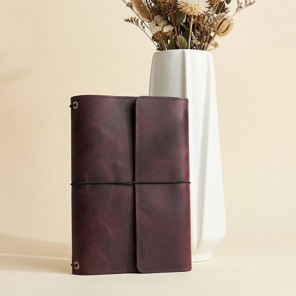 Brown leather notebook with a white vase containing dried flowers on a beige background