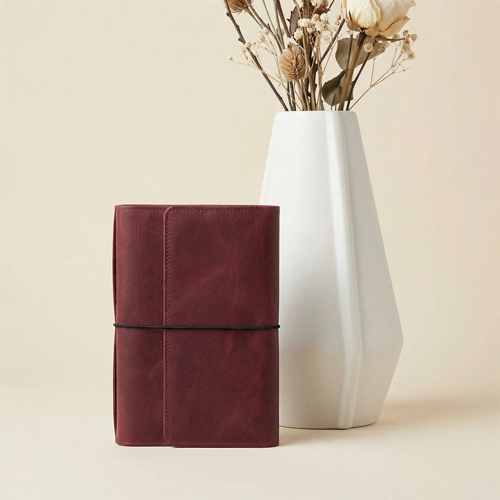 Maroon cylindrical container next to a white vase with dried flowers on a beige background
