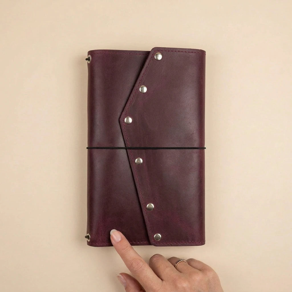Brown leather journal with silver rivets held by a hand on a beige background