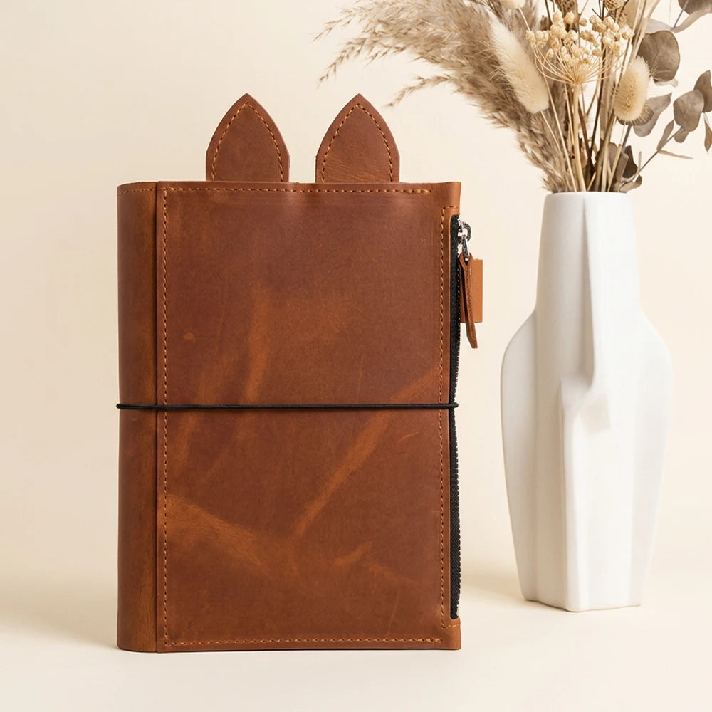 Rustic genuine leather notebook cover featuring zip pocket, pen holder, decorative ears, and elastic bands.