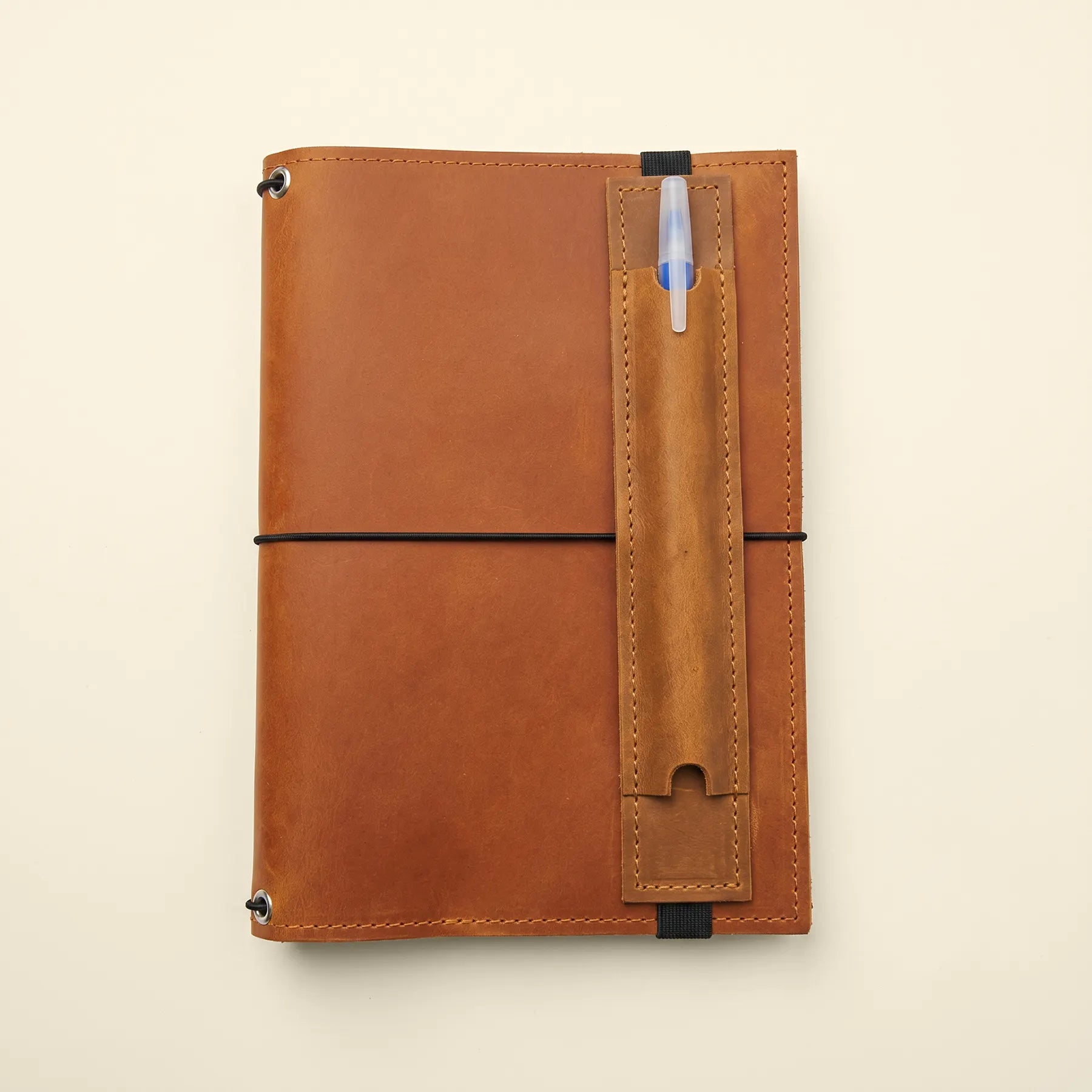 Refillable journal accessory featuring genuine leather pen holder with elastic notebook strap.
