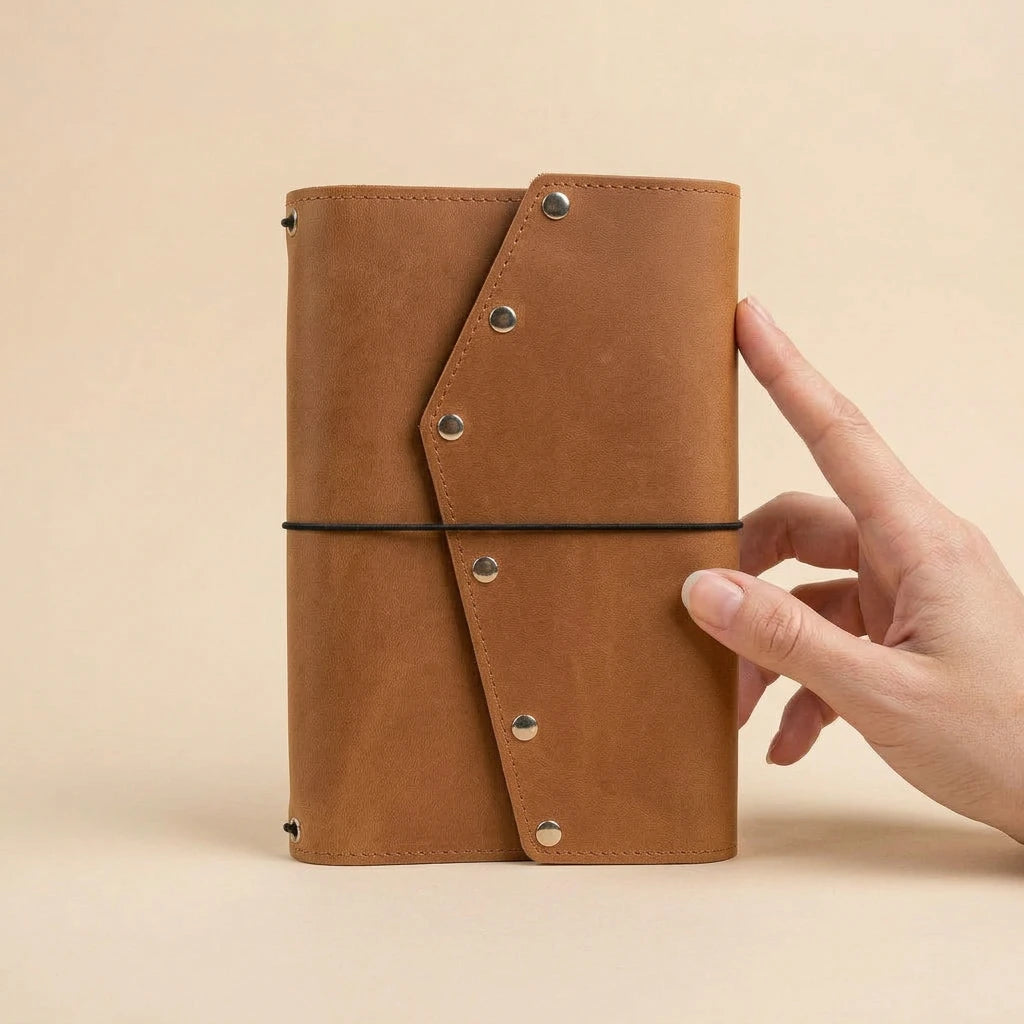 Brown leather notebook held by a hand on a beige background