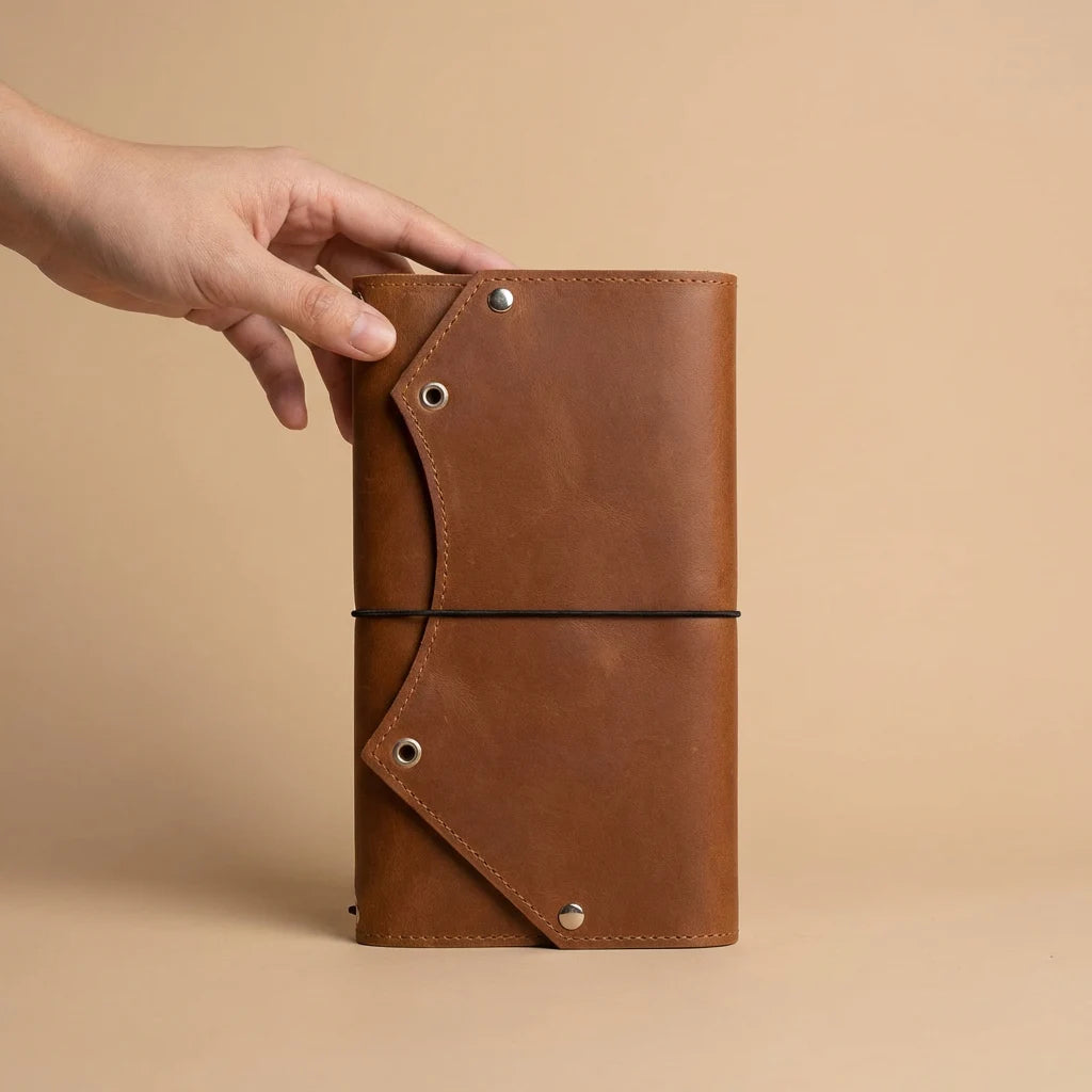 Brown leather notebook held by a hand against a beige background