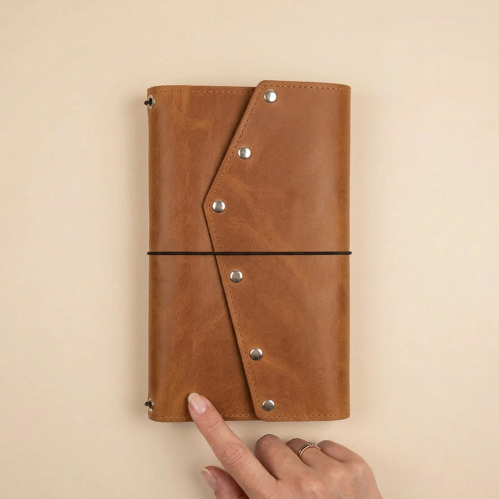 Brown leather journal with metal rivets held by a hand on a beige background