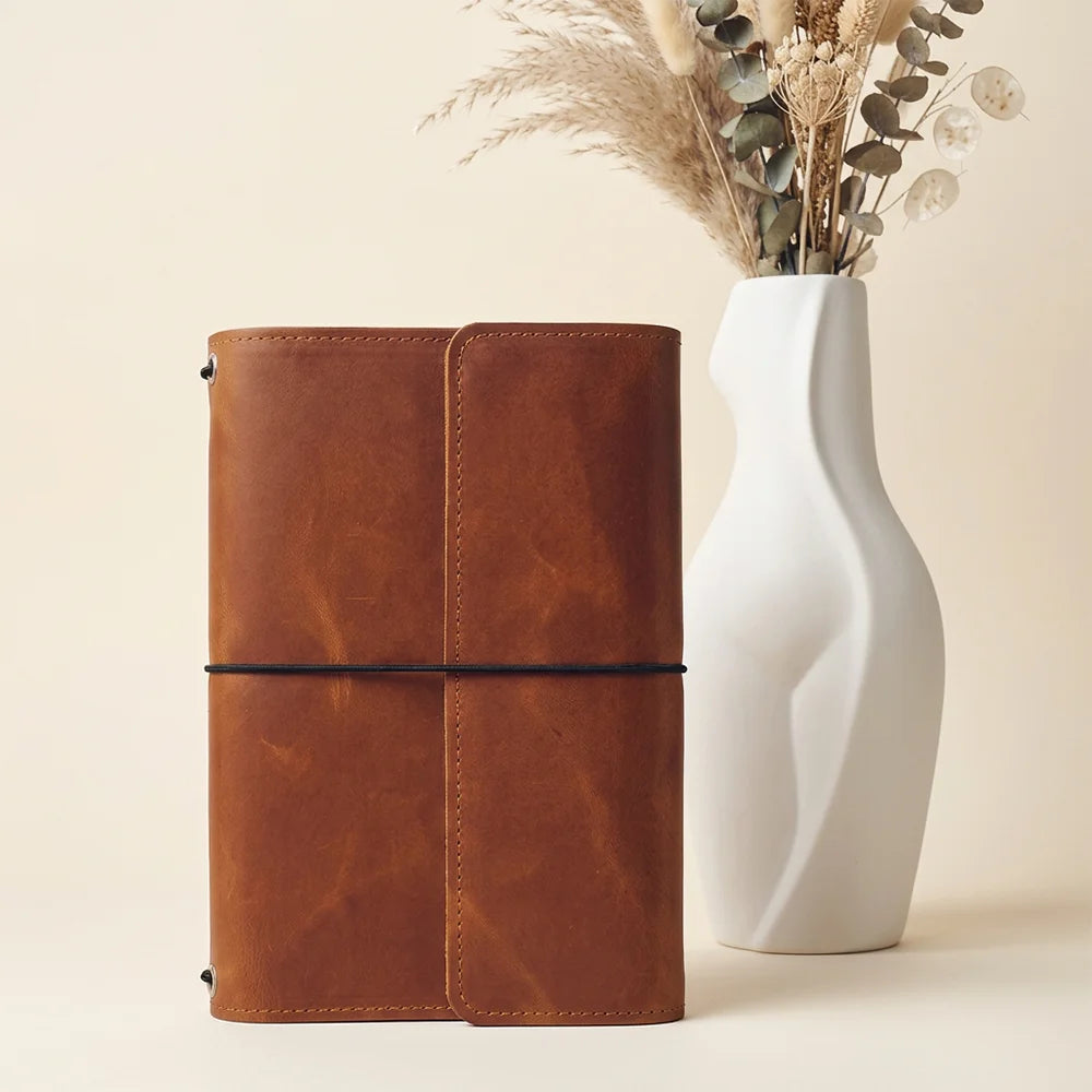 Distressed leather notebook cover featuring inner storage slots and a dedicated writing tool loop.
