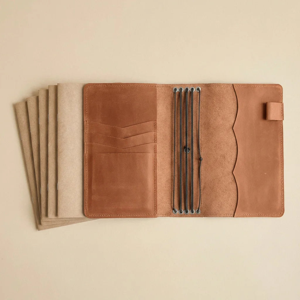 Brown leather journal cover with pen holder on a beige background