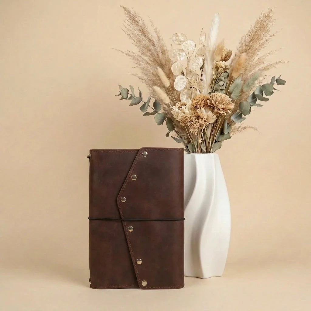 Brown leather notebook with a white vase containing dried flowers on a beige background
