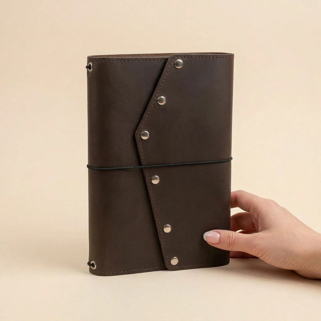 Brown leather notebook held by a hand on a beige background