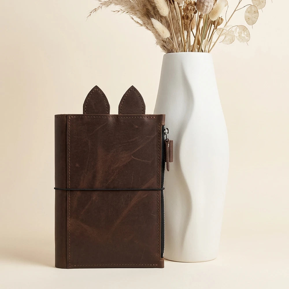 Leather journal holder featuring smooth panels, elastic cords, and metal eyelets.