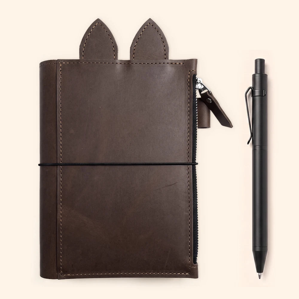 Rustic leather notebook cover with large zippered pocket, pen holder, decorative ears, and elastic closures.