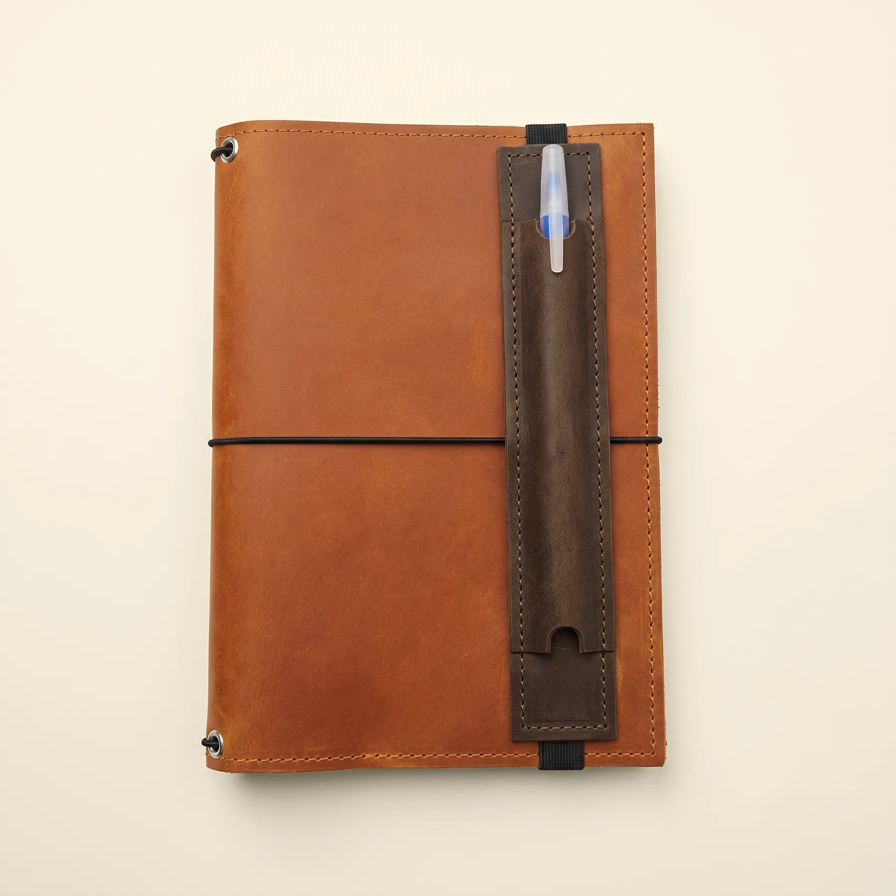 Leather notebook accessory with secure pen loop and wide elastic mounting strap.