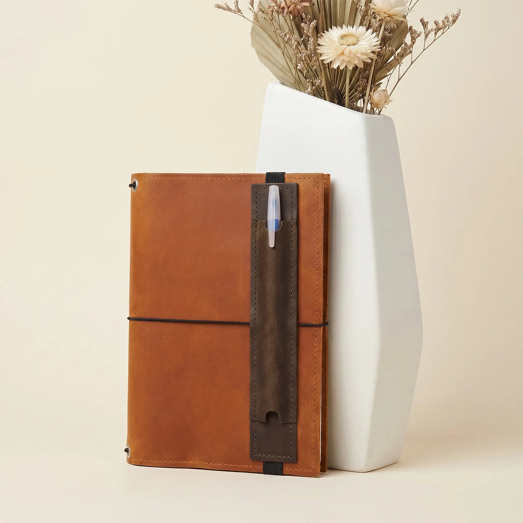 Slim leather pen loop accessory keeping writing tools securely attached to notebooks.
