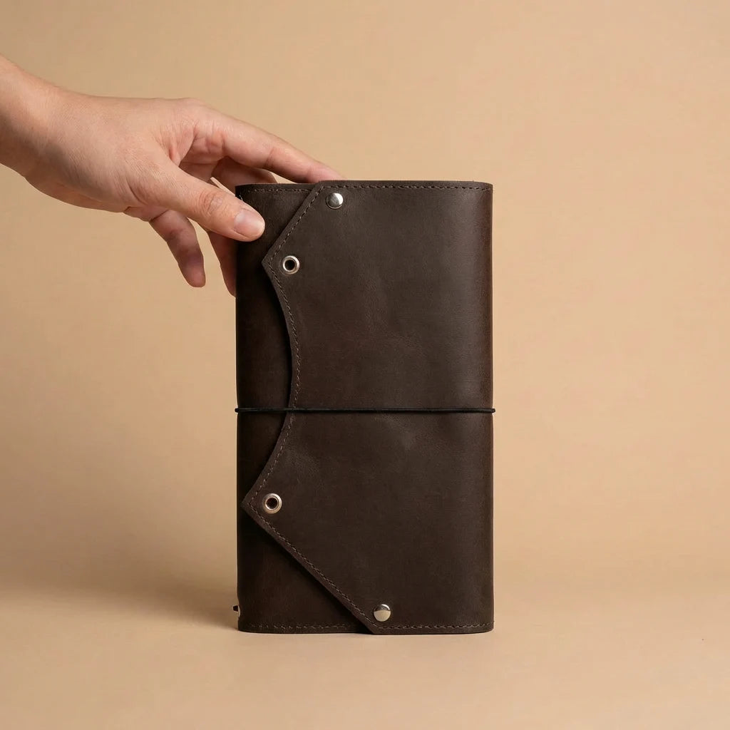 Brown leather notebook held by a hand on a beige background
