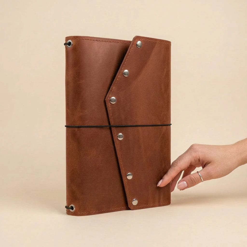 Brown leather notebook with metal rivets held by a hand on a beige background