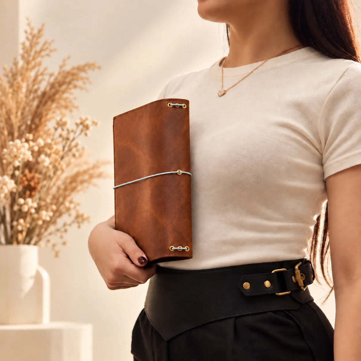 Young woman holding a handmade natural leather notebook cover in a simple lifestyle setting.