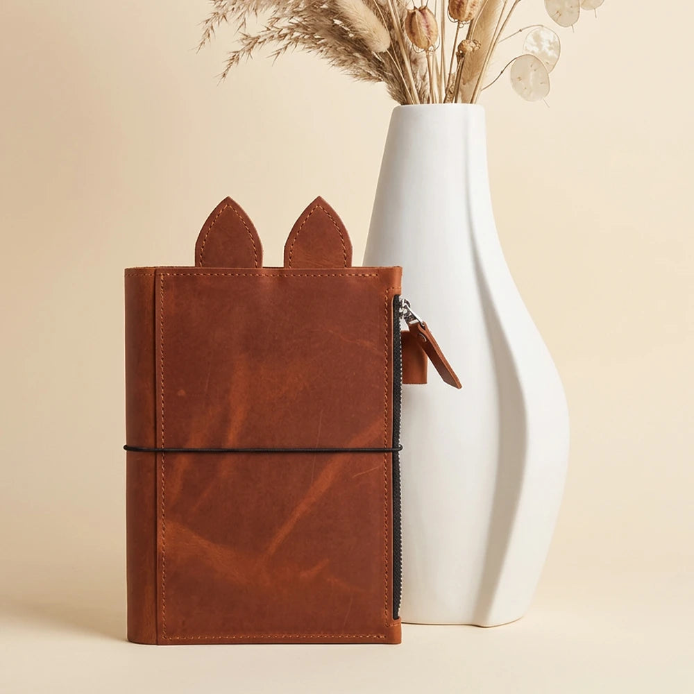 Leather notebook organizer featuring stitched edges, decorative ears, and three elastic cords.