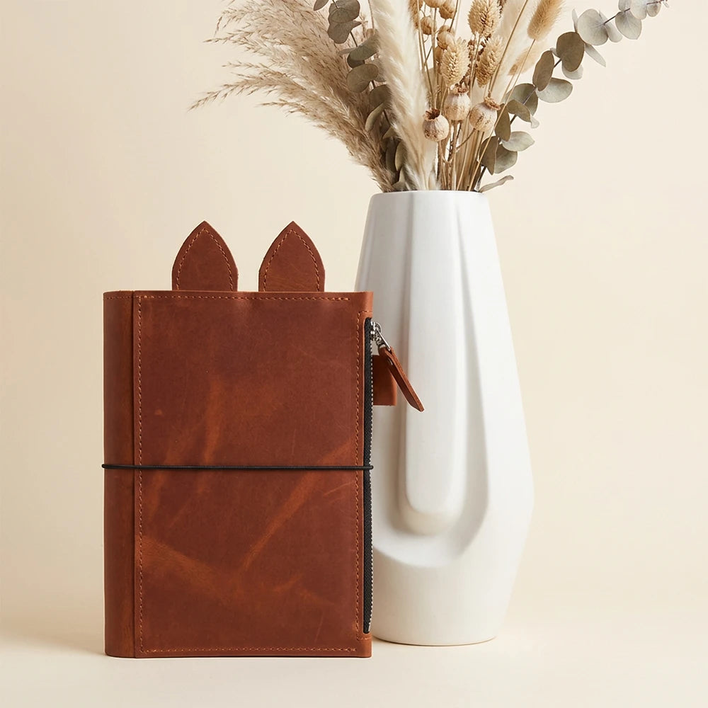 Refillable genuine leather organizer with zippered pocket, pen loop, decorative ears, and elastic bands.