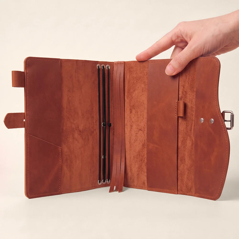 Handmade leather notebook cover with organized pockets, elastic pen loop, integrated bookmark, and carry handle.