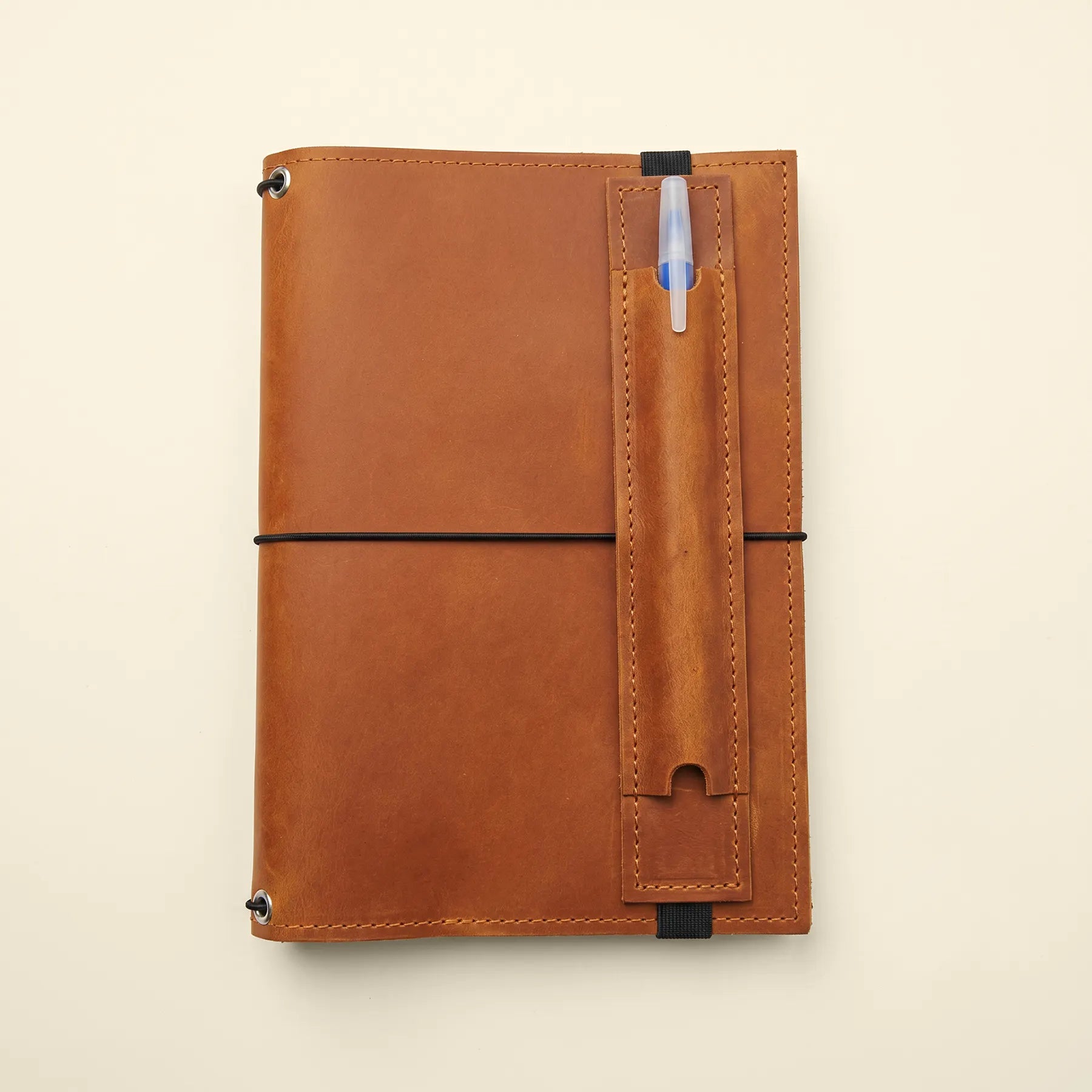 Handmade leather pen loop accessory with stretch band for journals and planners.