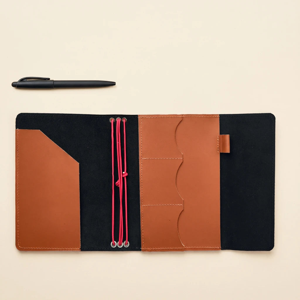 Handcrafted leather notebook cover with elastic fastening, interior pockets, and attached pen loop