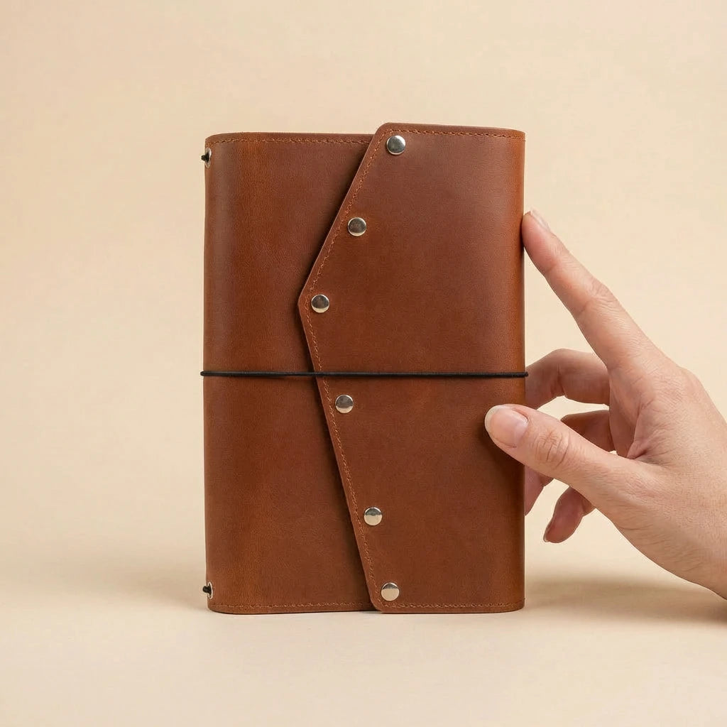 Brown leather notebook held by a hand on a beige background