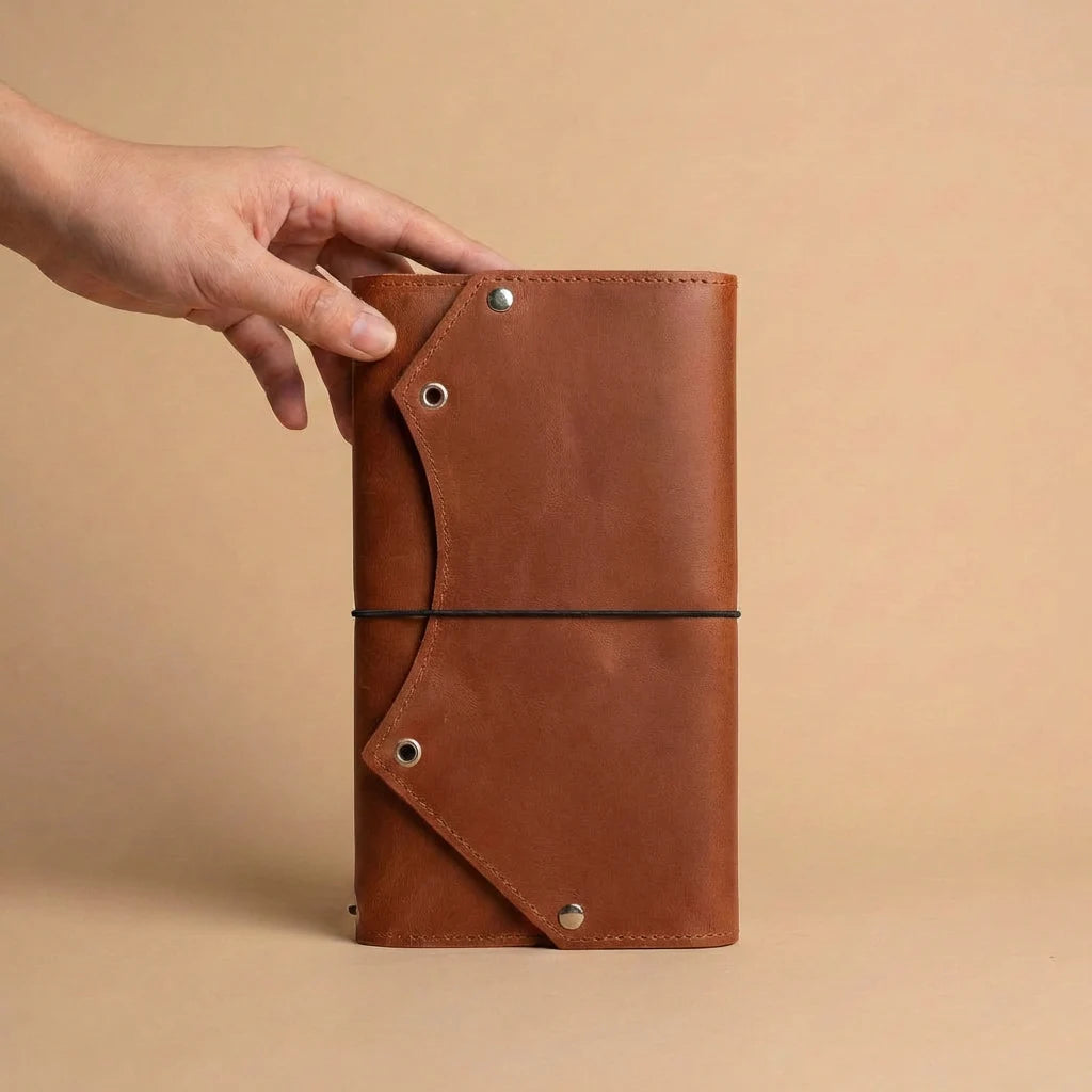 Brown leather notebook held by a hand against a beige background
