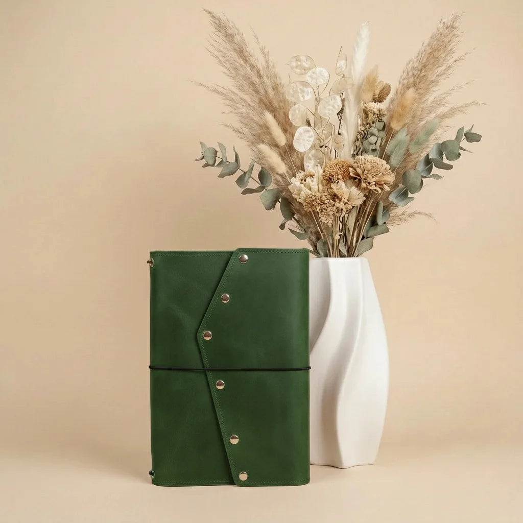 Green leather notebook with a vase of dried flowers on a beige background