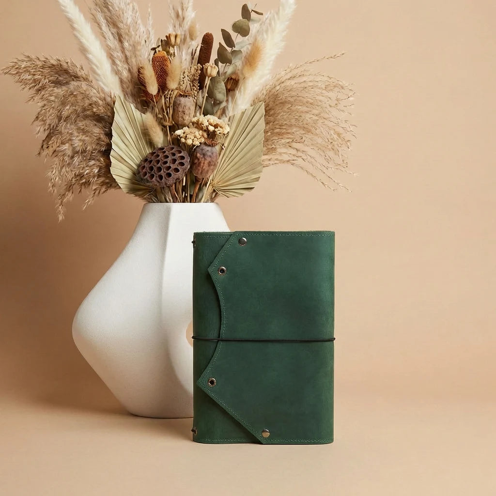 Green leather notebook with dried plants in a white vase on a beige background