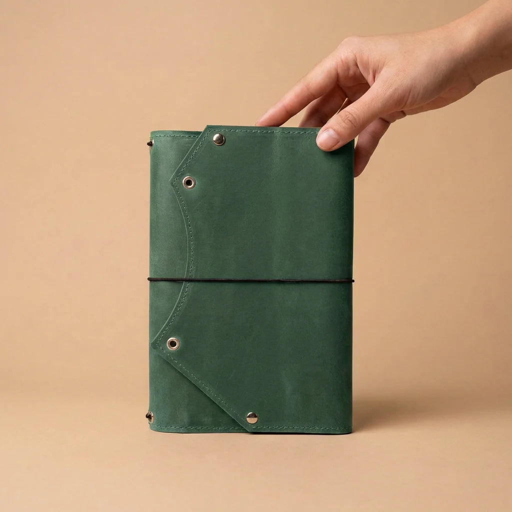 Green leather notebook held by a hand against a beige background