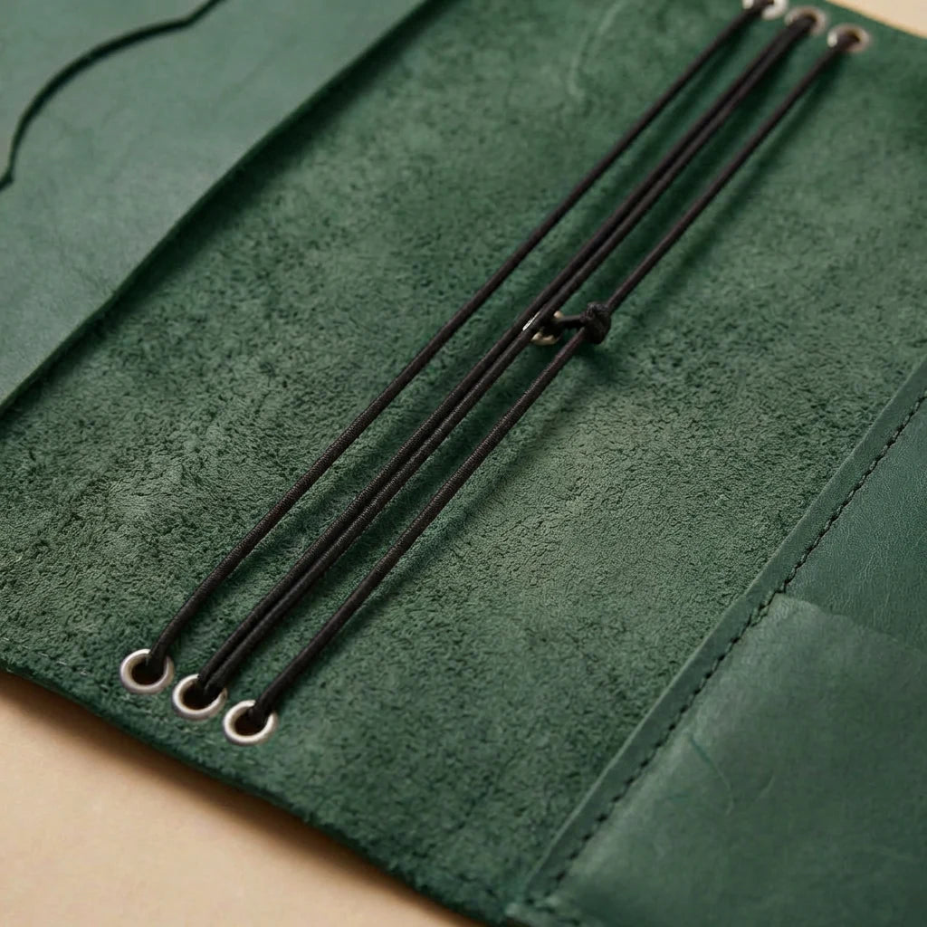 Close-up of green leather journal cover with black straps on a beige background
