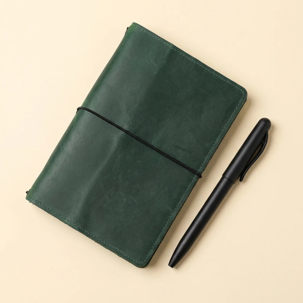 Green leather notebook with a black pen on a beige background
