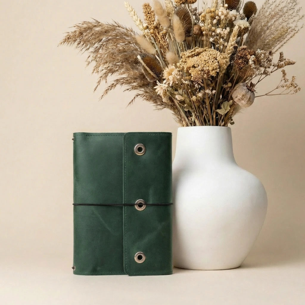 Green leather notebook and white vase with dried flowers on a beige background