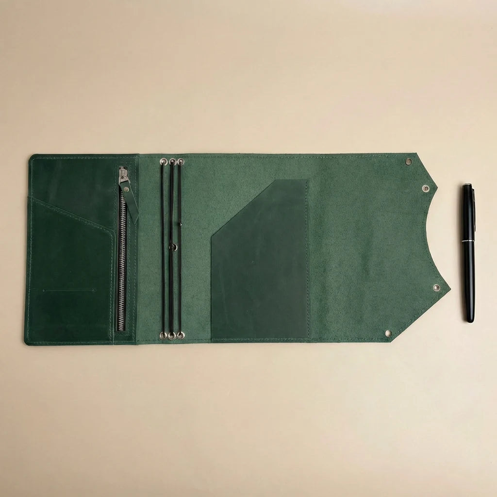 Green leather journal cover with zippers and a pen on a beige background