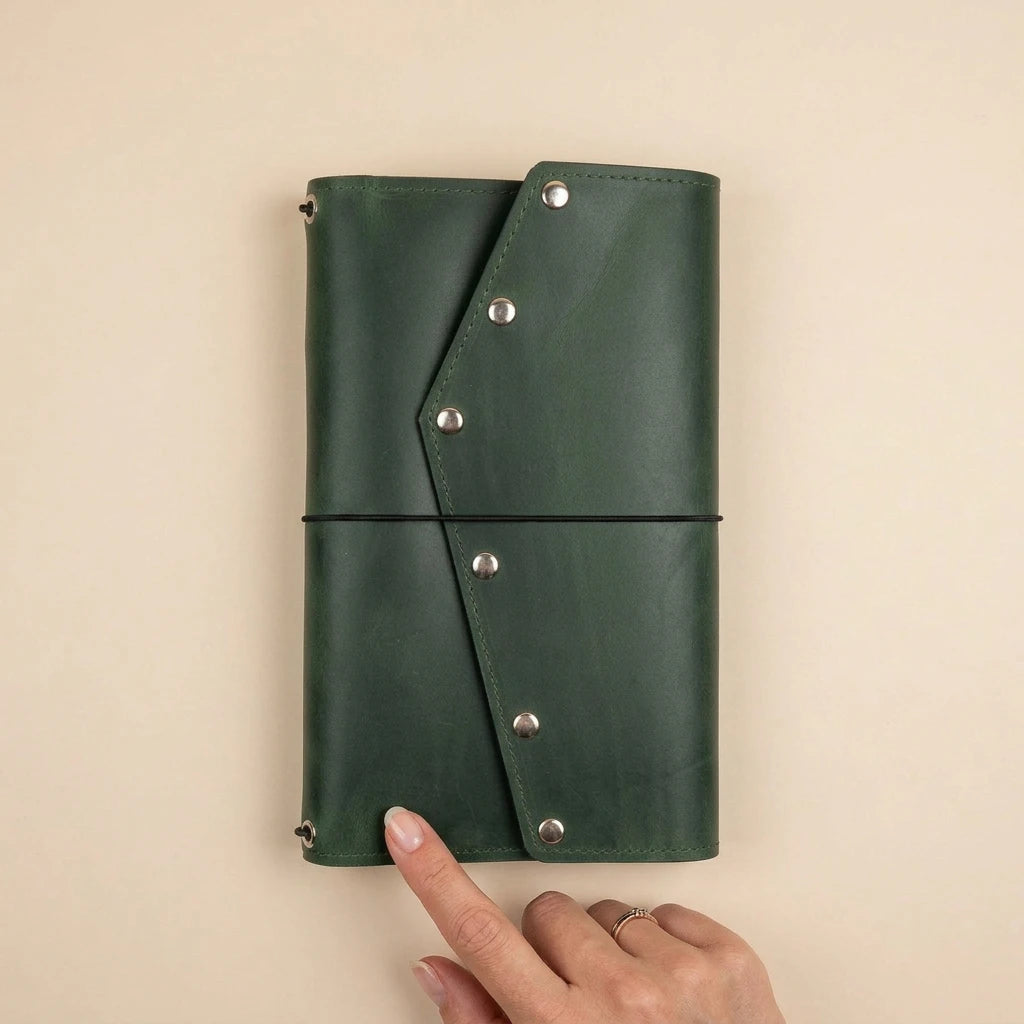 Green leather journal with metal studs held by a hand on a beige background