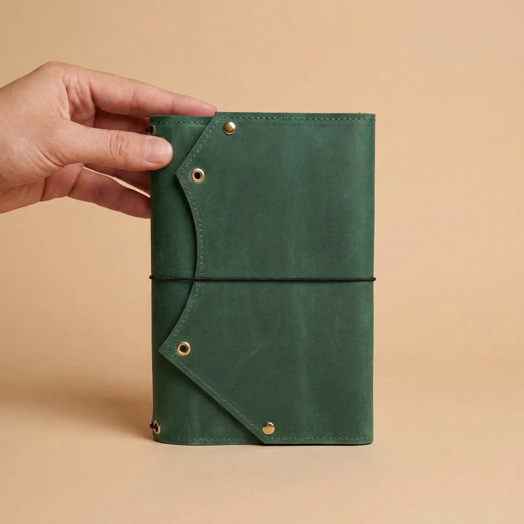 Green leather notebook held by a hand on a beige background
