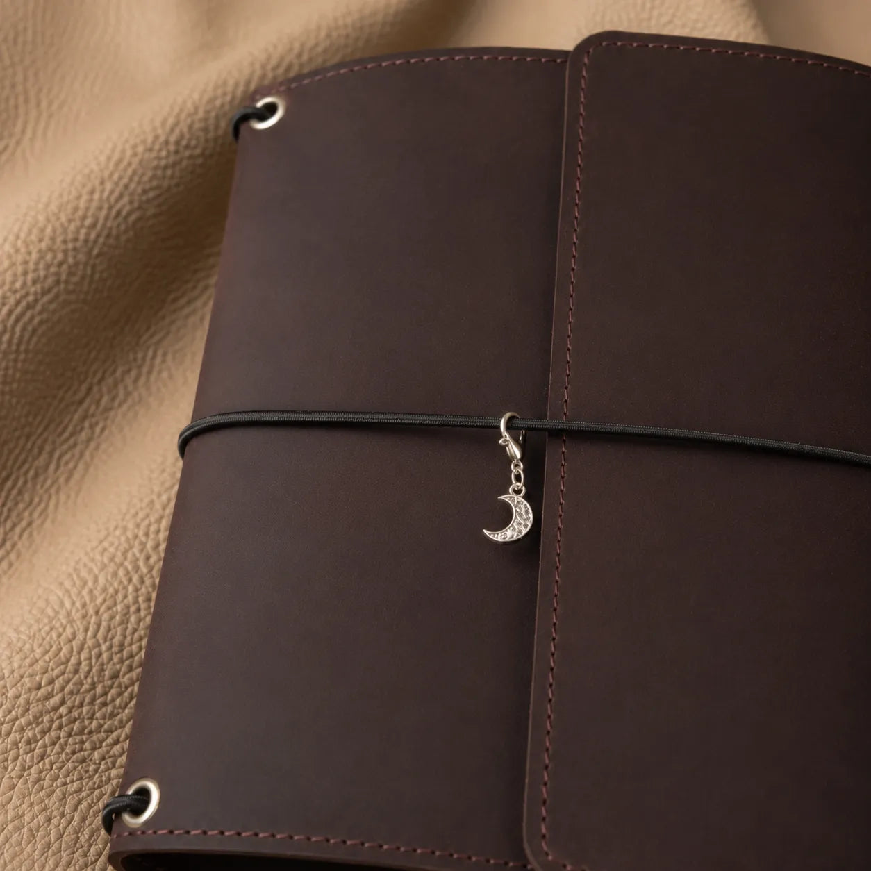 Crescent moon journal charm attached to leather notebook elastic bands, elegant handmade planner accessory.