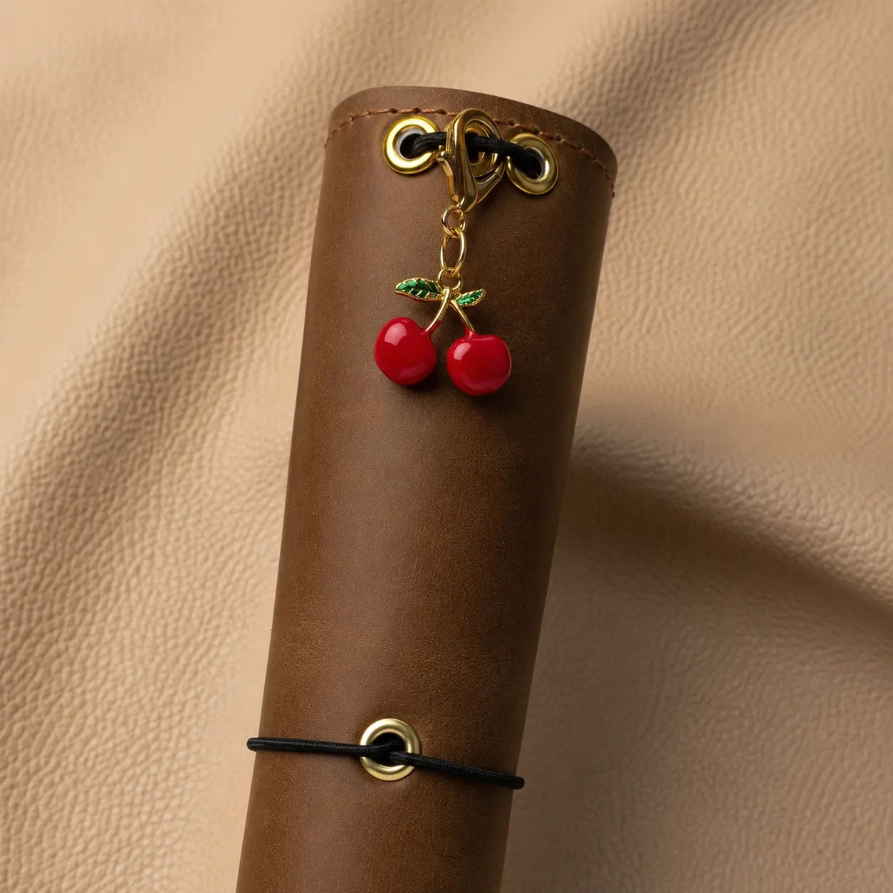 Cherry journal charm with metal attachment clipped onto elastic band inside a leather notebook cover.