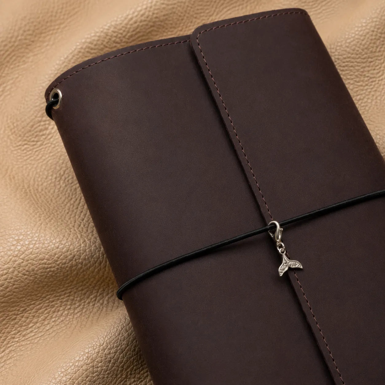 Decorative whale tail beaded journal charm clipped onto elastic bands of a leather notebook.