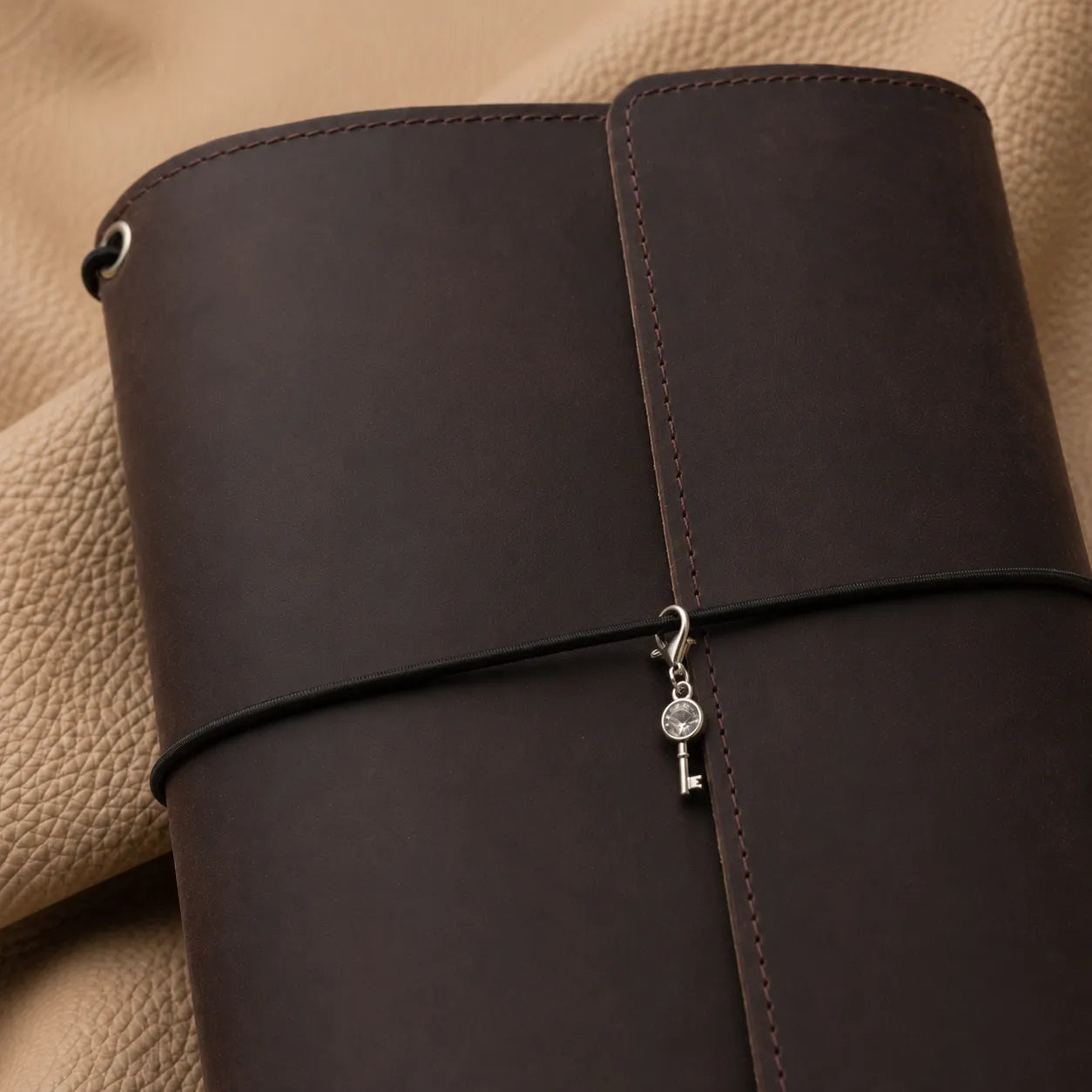 Metal key journal charm attached to an elastic band on a genuine leather notebook.