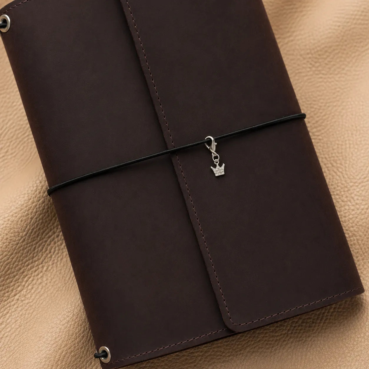 Crown-shaped journal charm attached to elastic bands, elegant metal accessory for leather notebooks.
