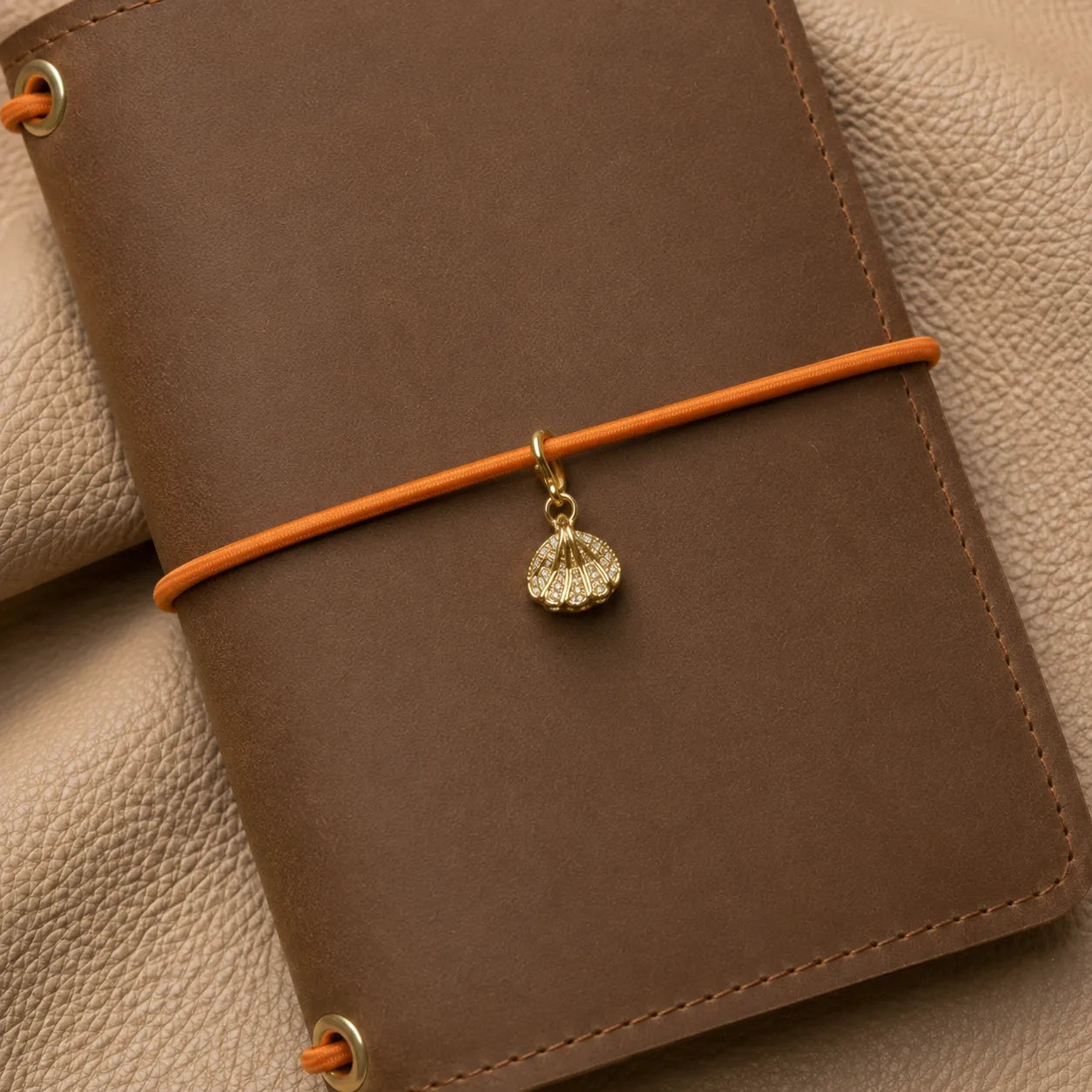 Shell-shaped journal charm attached to notebook elastic bands, elegant decorative planner accessory.